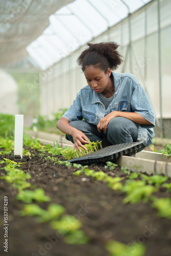 Young African woman planting seedlings in greenhouse, focused on sustainable agriculture and organic farming, surrounded by green plants and soil.