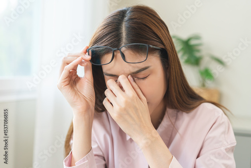 Fotografie Eye problem concept, fatigue asian young woman tired eyes, irritated rubbing nose, relief vision pain after work on laptop computer, eye strain, hand holding glasses, suffer migraine, bad blurry