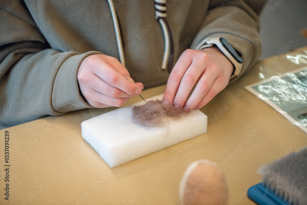 Obraz premium Close-up of hands using needle felting technique, meticulously shaping wool fibers on a foam block, creating intricate designs with precision and artistry