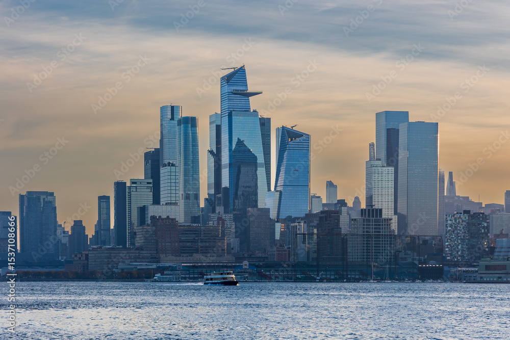 Fototapeta premium Early morning ferry travels across the Hudson River with the sleek skyscrapers of Hudson Yards in the distance.