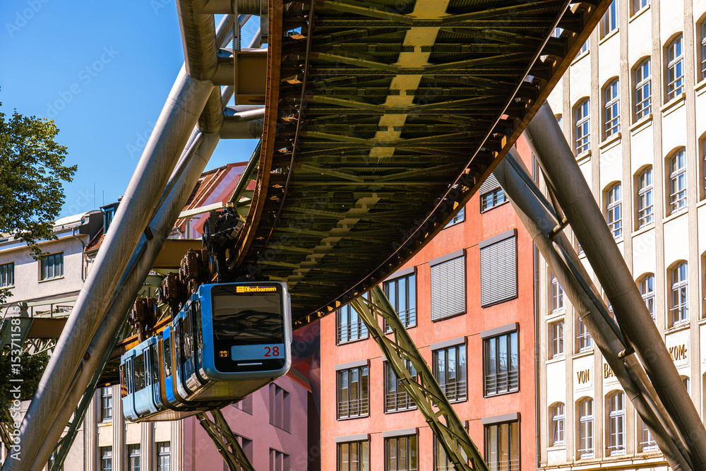 Fototapeta premium Eine Schwebebahn fährt zwischen alten Industriegebäuden in der Nähe der Haltestelle Kluse, Wuppertal, Deutschland