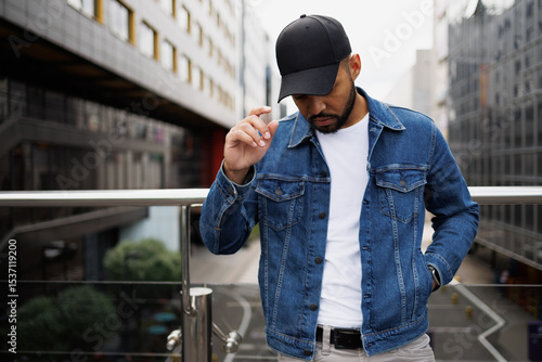 Young african american man in denim jacket and baseball cap standing on urban street