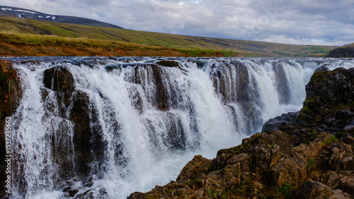 Majestic waterfalls cascade down rocky cliffs in Kolugljufur Canyon, showcasing Iceland breathtaking natural beauty. The lush surrounding landscape complements the serene atmosphere.
