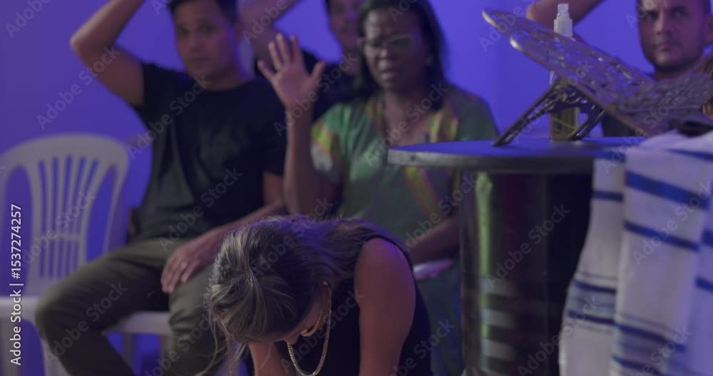 African American woman raises hand in prayer behind kneeling Hispanic woman, surrounded by Latin worshippers in solemn moment during evangelical church service African American woman raises hand in prayer behind kneeling Hispanic woman, surrounded by Latin worshippers in solemn moment during evangelical church service