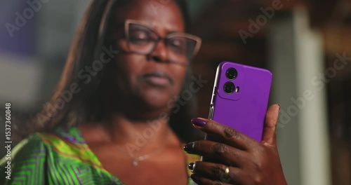 African American woman squinting at smartphone screen with puzzled expression, reacting to unexpected message in dimly lit evening environment