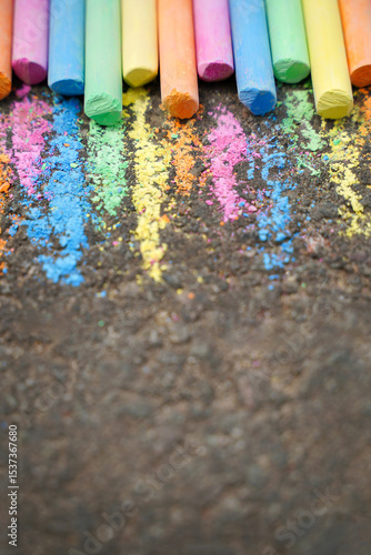 Vibrant chalk art on asphalt. Colorful set of brightly hued chalk sticks arranged on a dark asphalt surface with traces of their pigments creating a lively, textured background. Childhood creativity