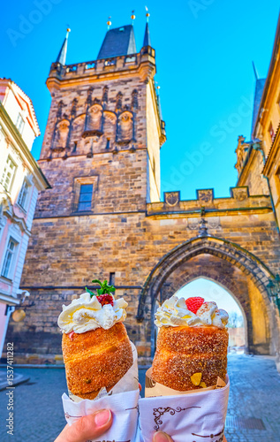 Trdelnik spit cake with cream and toppings against Mala Strana Bridge Tower, Prague, Czechia