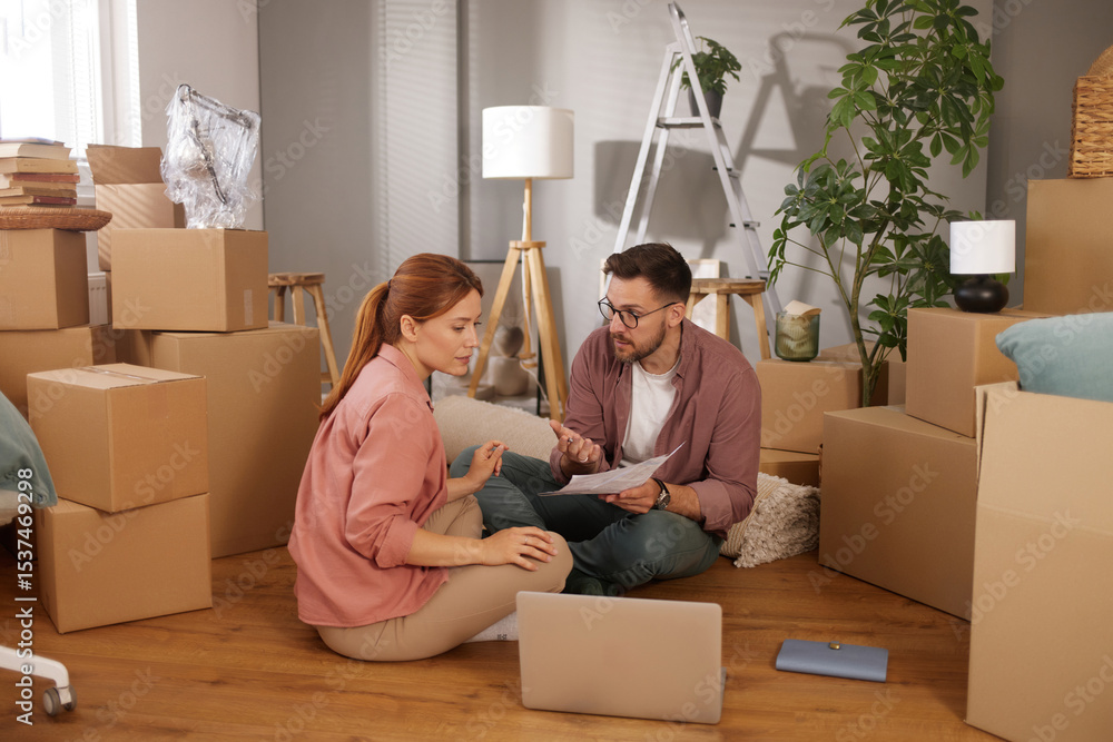 A couple is seated on the floor amidst several cardboard boxes in their new home, discussing moving logistics while reviewing paperwork on a laptop. A couple is seated on the floor amidst several cardboard boxes in their new home, discussing moving logistics while reviewing paperwork on a laptop.