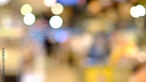 A blurry image of a crowded shopping mall with people walking around and shopping. Scene is busy and bustling, with people going about their daily activities