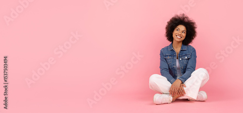Schilderij op canvas Young Black woman sitting cross legged on floor, looking up with a thoughtful an