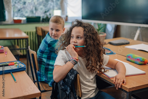 Fototapet Thoughtful elementary school student chewing on pencil in classroom