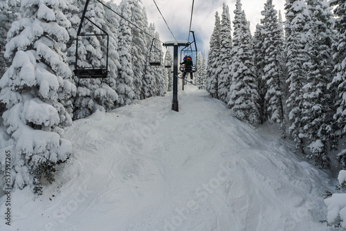 Snowboarder/skier riding a chairlift through the snowy trees at Steamboat Springs ski area in the winter