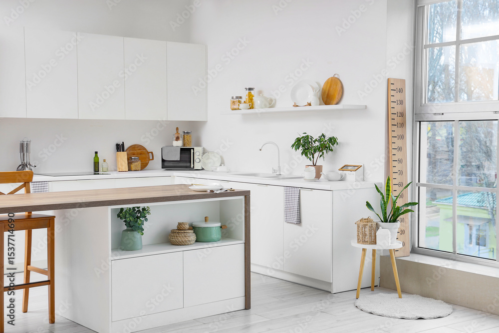 Fototapeta premium Interior of modern kitchen with wooden stadiometer, houseplants, microwave and kitchenware on counter