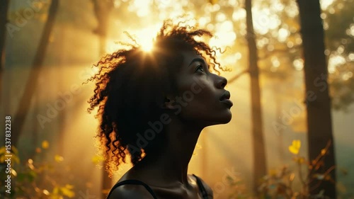 Portrait of a thoughtful young woman standing in a forest at sunrise, with warm golden light and peaceful natural surroundings.