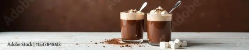 Two elegant hot chocolate glasses, marshmallows, silver spoons Dark brown wall, white wood table , white table, steam, rustic