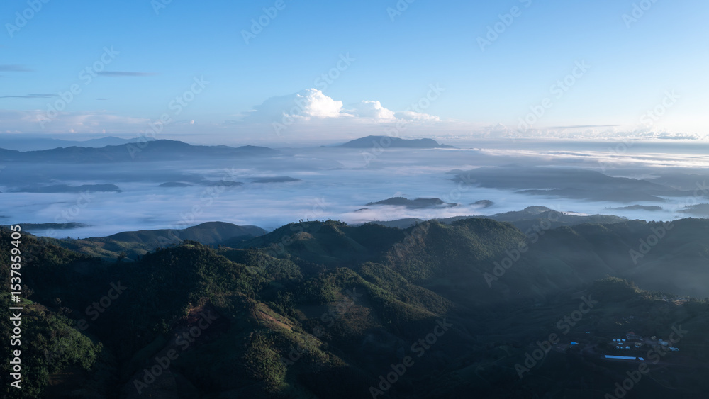 Obraz premium wide-angle view of vast morning mountain scenery with a sea of mist covering the valleys below, contrasting with the blue sky and soft sunlight, depicting the grandeur and tranquility of nature.