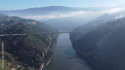 Wallpaper Mural Aerial view of a long, modern bridge spanning a wide river valley, with lush green, misty mountains rising dramatically on both sides under a hazy sky. Torontodigital.ca