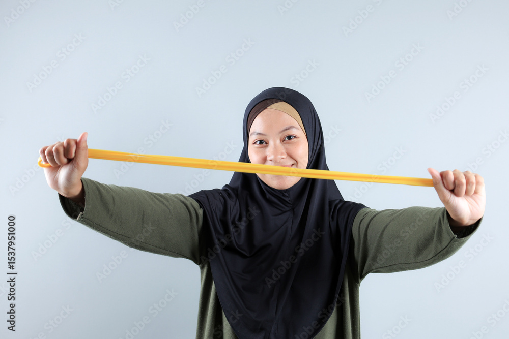 Young Asian Hijab Woman Stretching Yellow Resistance Band for Hand Pilates Exercise Young Asian Hijab Woman Stretching Yellow Resistance Band for Hand Pilates Exercise