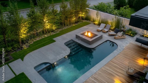 Bird's-eye view of luxury backyard with L-shaped pool, wooden deck, modern fire pit area, and soft garden lighting