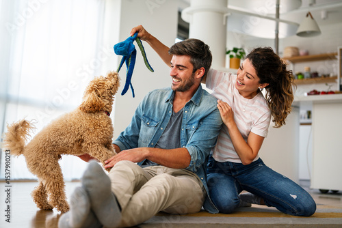 Foto Happy couple playing with dog, having fun on floor at home