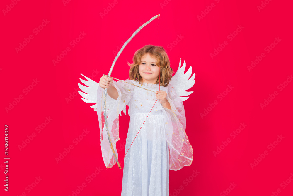Fototapeta premium Angel kid shoots a love arrow from a bow on Valentines Day. Angel child. Isolated studio shot. Cute kid with angel wings. Cupid, valentines day concept.