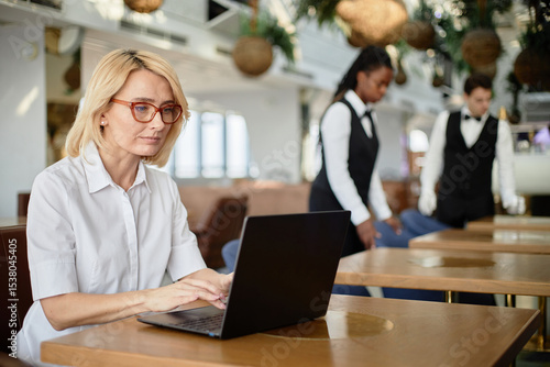 Foto Caucasian middle aged woman working on laptop at restaurant table, Black woman a