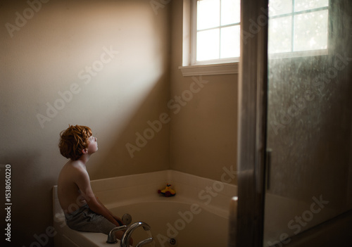 Soft light falls on boy during quiet indoor bath scene