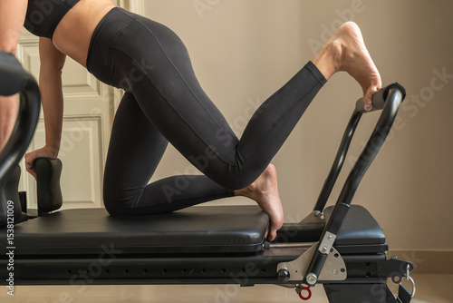 Canvastavla Athletic woman doing a hip flexor lunge stretch on a pilates reformer machine in a studio