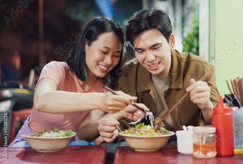 Couple enjoying traditional Vietnamese cuisine at a bustling Hanoi street food stall during the evening