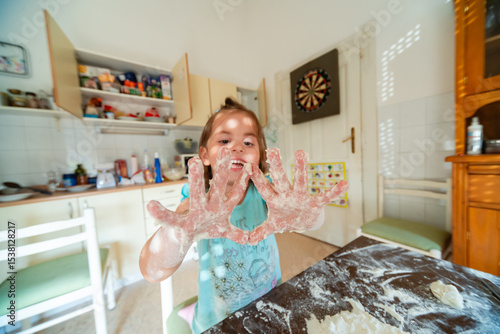 Fotografía Little girl making dough in messy kitchen, showing floury hands