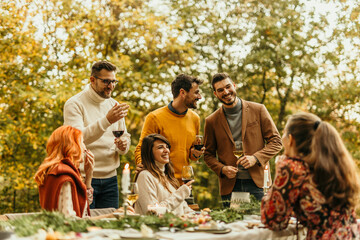 Friends enjoying celebrating thanksgiving dinner outdoors in beautiful autumn forest