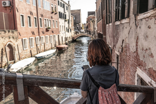 Tourist using smartphone and enjoying view of venice canal and bridge