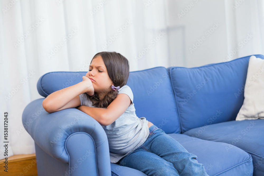 Girl child sitting home on blue sofa resting elbow gazing sideways with white pillow, copy space Girl child sitting home on blue sofa resting elbow gazing sideways with white pillow, copy space