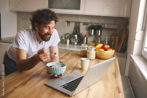 Foto A man is smiling as he eats from a bowl of cereal while seated at a wooden kitchen counter
