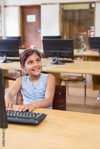 Indian girl child typing on keyboard at school computer lab with desktop monitor and wooden desk