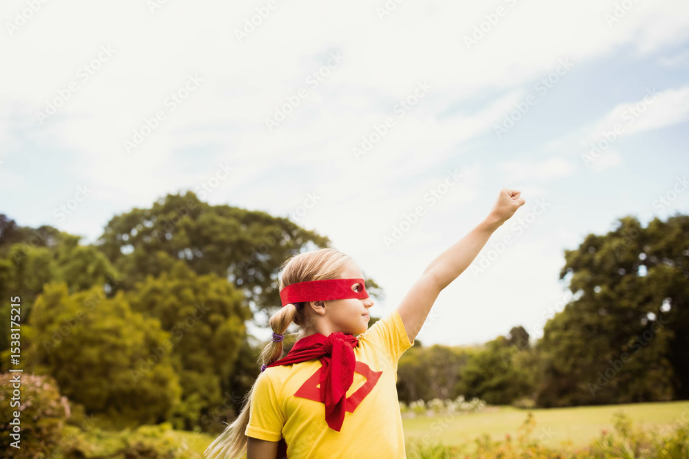 Female child posing as superhero on grassy park lawn wearing red cape and eye mask Female child posing as superhero on grassy park lawn wearing red cape and eye mask