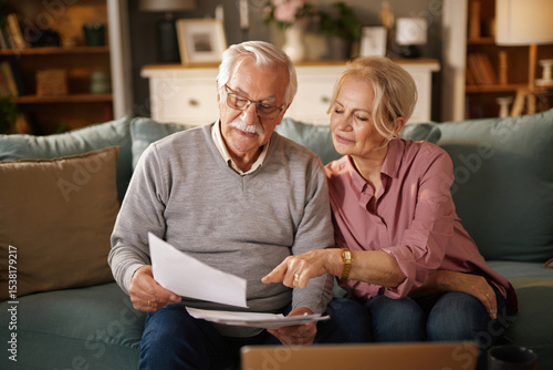 Papier peint An elderly couple, sitting on a sofa, reviews paperwork and a laptop