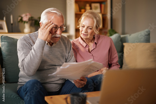 Bild auf Leinwand An elderly man and woman are sitting together on a sofa inside their home