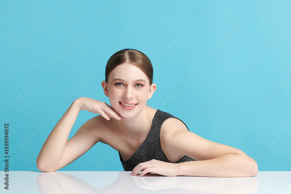 Fototapeta premium A beautiful young woman with clean, fresh skin against a blue background. Skincare, facial treatment, cosmetology, beauty, and spa. An elegant portrait of an woman.