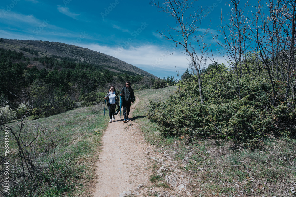 Obraz premium A couple enjoying a scenic hike on a nature trail in a mountainous area under clear blue skies.