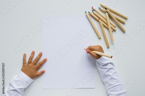Child drawing on blank paper with colored pencils on white background