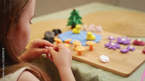 Child meticulously arranges colorful play dough figures on a wooden board, crafting a miniature garden scene