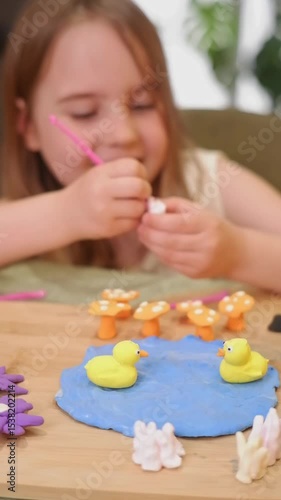 Young girl making polymer clay ducks and mushrooms on a pond