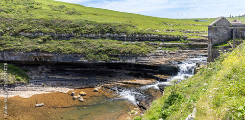 Fototapeta El Bolao Waterfall, with the water gently falling from the meadows to the sea, surrounded by rugged rocks