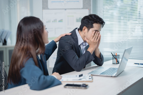Businesswoman providing comfort to her stressed male colleague in the office, demonstrating empathy and support during challenging times in the corporate environment