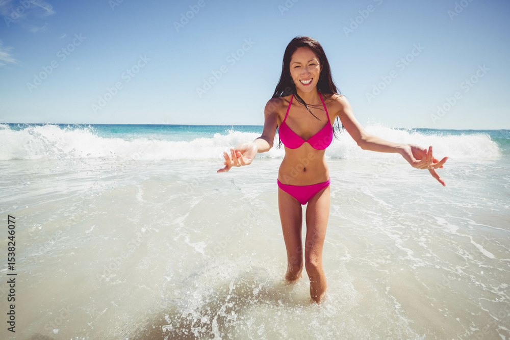Naklejka premium Chinese woman running through shallow surf on sandy beach producing waves in bright pink bikini