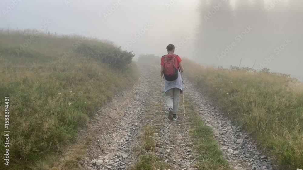 Woman from back with backpack hiking on foggy mountain trail Woman from back with backpack hiking on foggy mountain trail