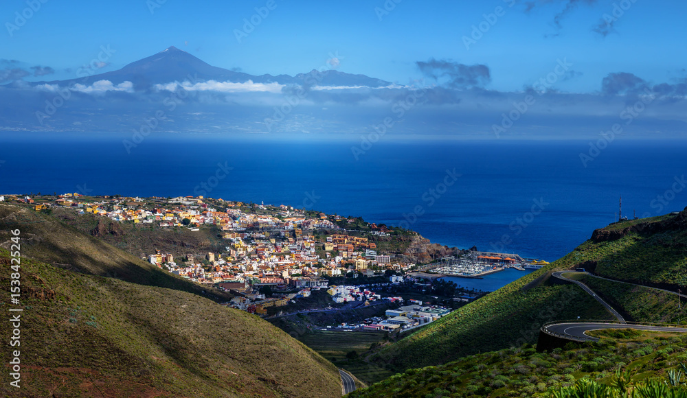 Fototapeta premium Blick am frühen Morgen vom Mirdor Lomada dell Capello auf die Inselhauptstadt San Sebastian de la Gomera; im Hintergrund der Pico del Teide (Tenerife) auf der rechten Bildseite eine Serpentinenstraße