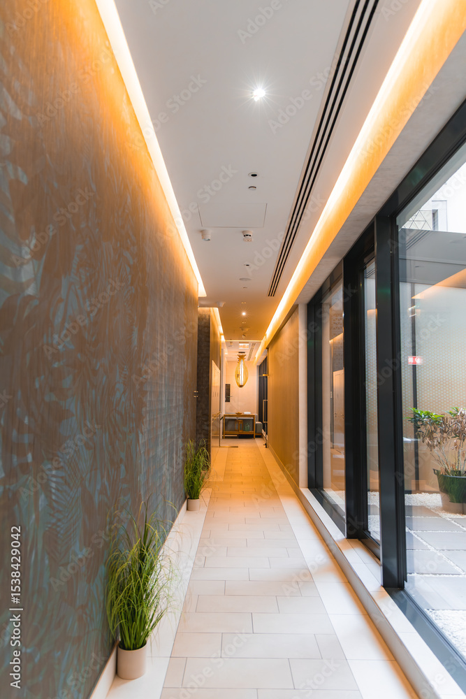 custom made wallpaper toronto digitalInterior hallway of a luxury hotel featuring recessed lighting, textured walls, glass panels, potted plants, and a neutral toned tiled floor.