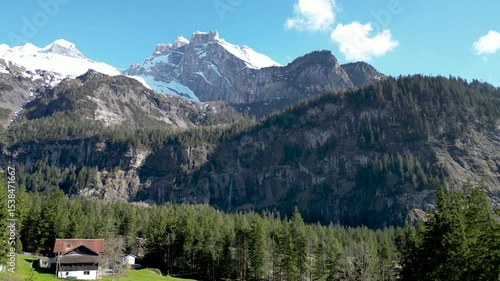 A 4k pan of the mountains surrounding Kandersteg in Switzerland during the spring. A small campsite can be seen in the foreground, There is snow on the mountains